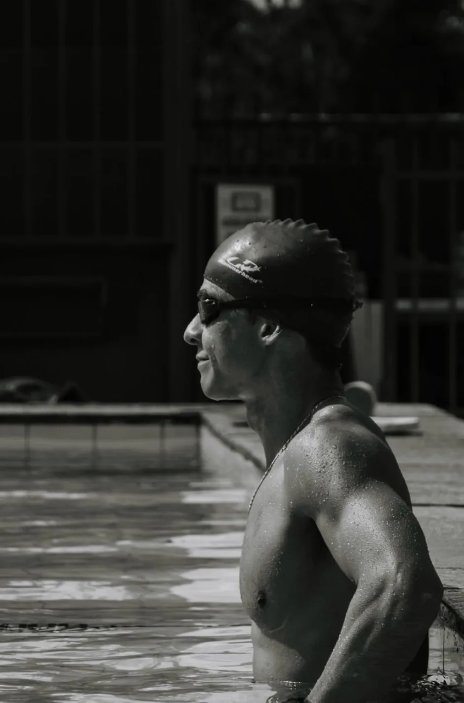 Perfil de nadador na borda da piscina sob luz dura, em preto e branco