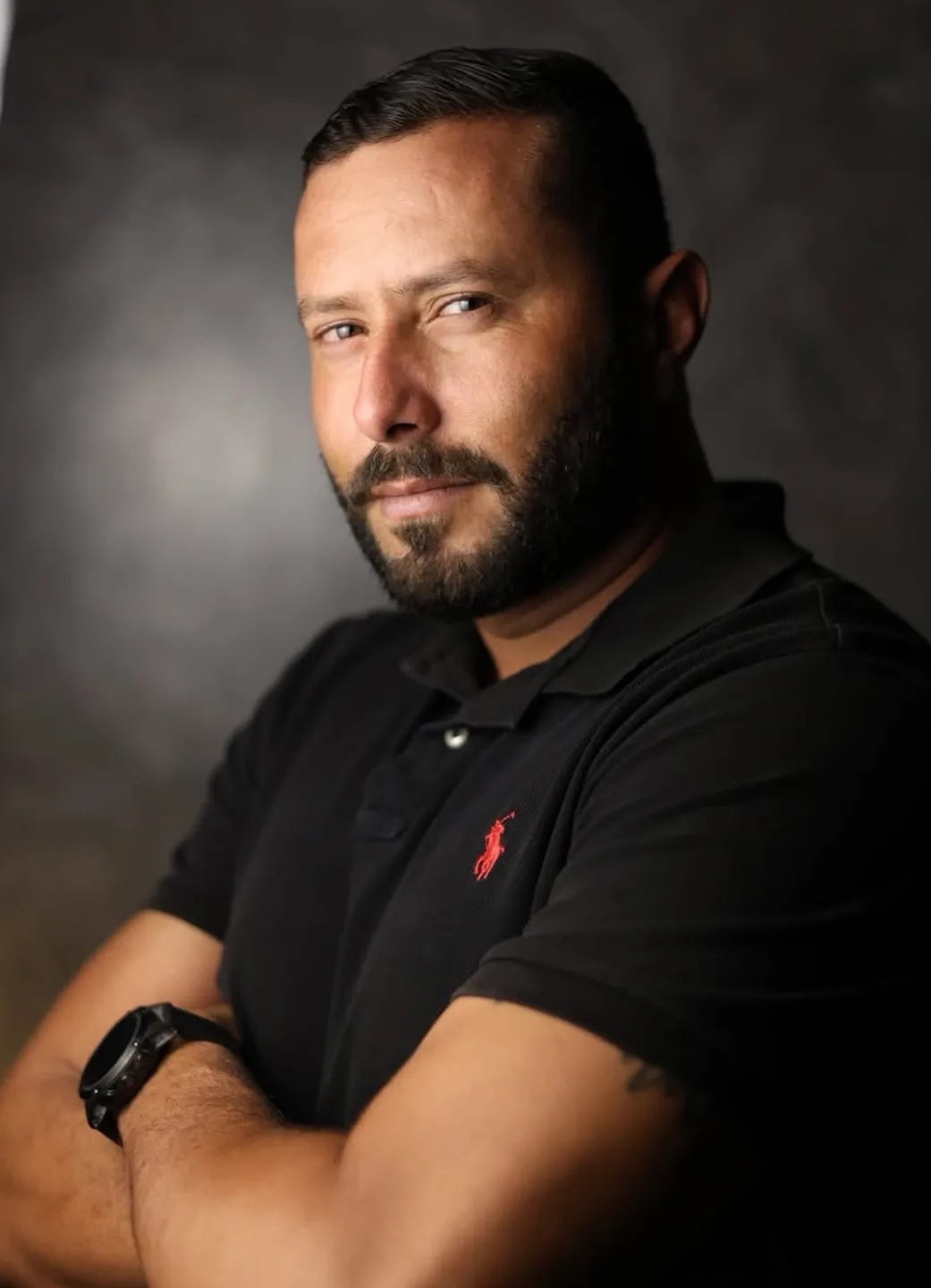 Retrato de estúdio do fotógrafo, de braços cruzados, sobre fundo escuro